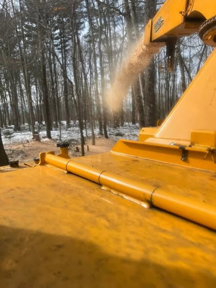 Close-up action shot of a yellow wood chipper's discharge chute spraying wood chips.
